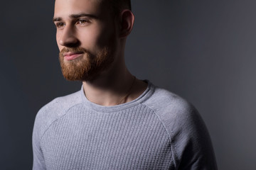 Obraz premium closeup, dramatic portrait of a handsome bearded guy of twenty-five years old, in a gray sweater, on a gray background. Casual style. Sweater, mens jacket. Smiling bearded young guy.