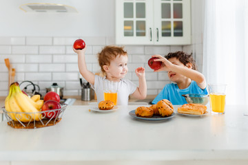 Happy children real brother and sister having breakfast with fruits in bright kitchen at the home