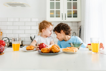 Obraz na płótnie Canvas Happy children real brother and sister having breakfast with fruits in bright kitchen at the home