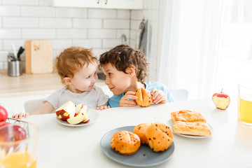 Happy children real brother and sister having breakfast with fruits in bright kitchen at the home