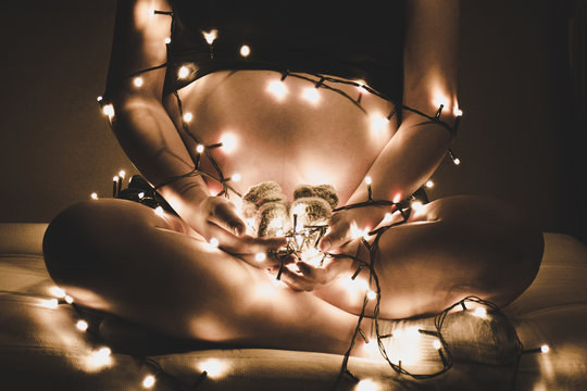 Embarazada cargando zapatitos de bebe con luces de navidad alrededor