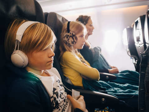 Caucasian boy with headphones sitting with sister and mother in airplane