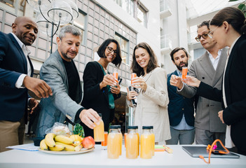 Smiling male and female business executives with juice outside office