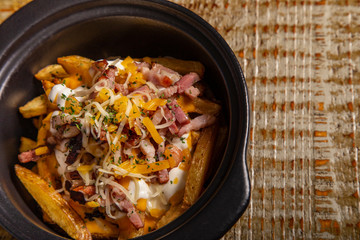 Casserole of rustic french fries with bacon and cheese on wooden background. Isolated image with...