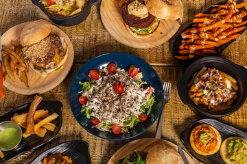 Wooden table with several dishes of Mexican food. Nachos, hamburgers, fried yucca and sweet potato potatoes.