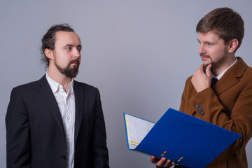 Portrait of two young business people in suits. The boss with a folder with documents in his hands...