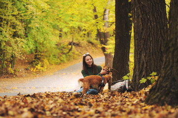 Young woman and her dog (American Cocker Spaniel) sitting in the park and throws up leaves.