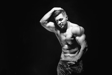 Obraz na płótnie Canvas Beautiful and health athletic caucasian muscular young man. Black-white photo. Dark background. Hand on head