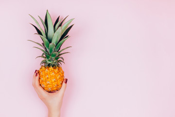 Hands with pineapple on stylish pink background.