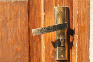 Close up of metal door handle on old wooden door in morning light.
