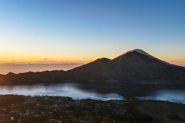 A morning golden hour seen from top of Mount Batur on Bali, Indonesia. There is Mount Rinjani in the back (Lombok) and Volcano Agung on the side. Fog in the valley. Mysterious and magical sunrise.