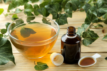 Ivy leaf and syrup in a bottle on a natural wooden table. Production of cough medicine with ivy extract. pharmaceutical industry