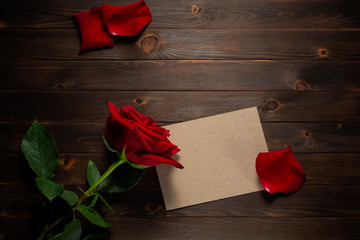 Empty card, red rose petals and red rose flower on rustic wooden background