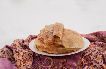 pancakes on a plate in winter next to a Russian handkerchief, pancakes on a plate against the...