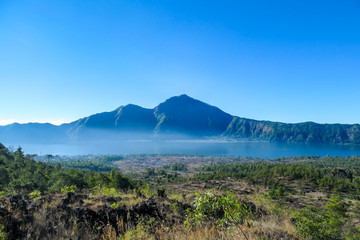An idyllic view from the top of Mount Batur on Mount Agung and the Danau Batur lake. There is a pathway along Batur volcano's rim. Volcanic landscape of Bali, Indonesia. Island hiking.