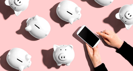 Piggy banks with person using a smartphone - flat lay