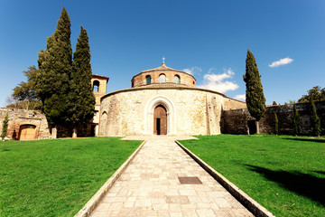 Fototapeta na wymiar Perugia, Italy - March 3, 2016: The small temple. External photo of the Church of San Michele Arcangelo, with the path that cuts the green lawn and the cypresses on the sides. Clear blue sky with smal