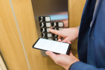 Close up of businessman using blank screen smartphone and pressing elevator button. Business and office building meeting concept. © zphoto83
