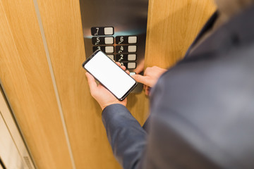 Close up of businessman using blank screen smartphone and pressing elevator button. © zphoto83