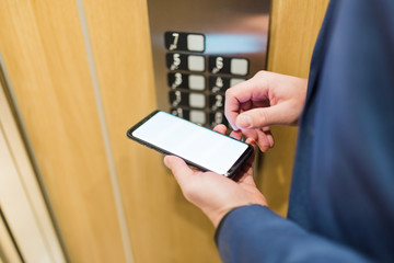 Close up of businessman using blank screen smartphone in elevator. Business and office building meeting concept.