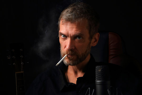 Portrait of a brutal man with a cigarette on the background of a microphone