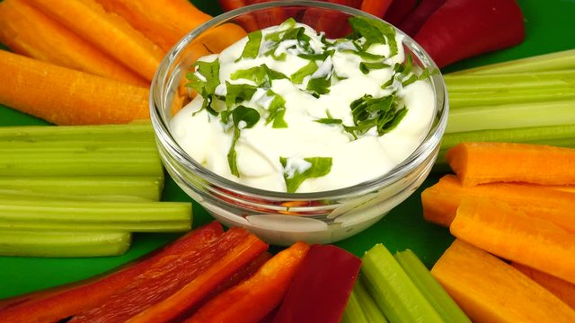 Raw sliced vegetables and white vegan sauce are laid out on a green dish, vegan snacks