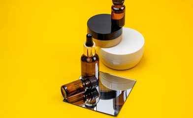 Set of cosmetic products with serum, face cream on a bright sandy yellow background with a mirror....