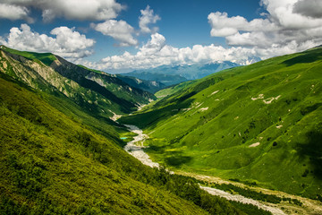 Stunning Adishi valley summer landscape seen from Chkhutnieri pass, Upper Svaneti, Georgia. Vibrant green slopes of Caucasus mountani range on a partially cloudy day.