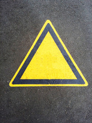 Blank triangle hazard, attention, warning, danger sign on the black asphalt. Empty triangular sticker in yellow and black colors. Use it in all your designs