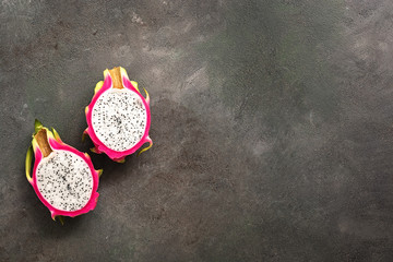 Halved dragon fruit pitahayas on a dark painted rustic background. Top view, flat lay, space for text.