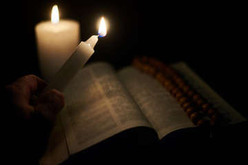A burning candle in a male hand and an opened bible, a book. The concept of faith in God,...