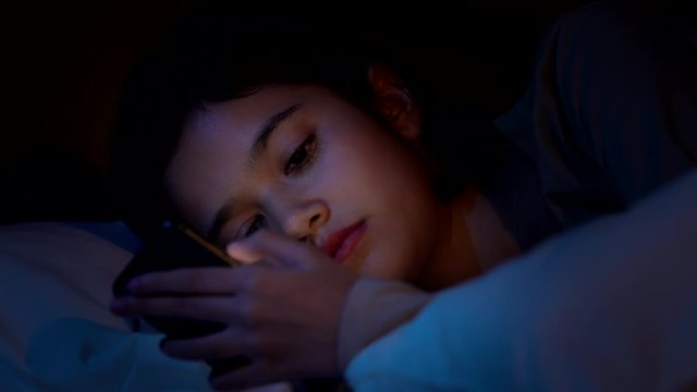 4K Depressed young beautiful Asian woman lying down on the bed and using smartphone. Insomnia sad woman looking at her smartphone. Smartphone addiction, depression symptoms and mental health concept.