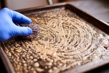 Cleaning a dirty oven pan with a metal sponge and detergent.