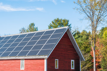 Solar panels on the roof of a red wooden barn on a sunny autumn day. Concept of alternative energy....