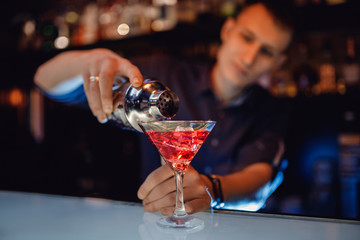 Barman is preparing mix cocktail in shaker of red alcohol and ice glass, bar counter