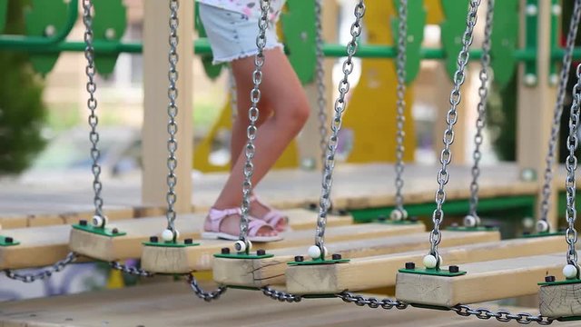 A child with pink shoes is balancing and playing on the colorful playground. Baby feet go over the staggering bridge