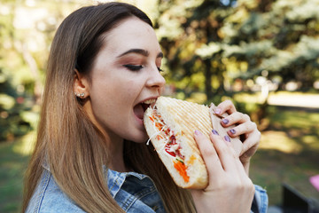 A hungry girl bit off a sandwich in park and covered her eyes with pleasure