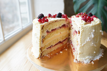 Two halfs of tasty cake with jam, cream and berries on wooden table near the window