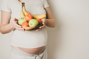 Pregnant belly, woman with healthy food, bowl of fruits in hands. Copy space.
