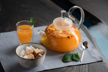 transparent teapot with sea buckthorn tea on a table with a sugar bowl devices and mint leaves