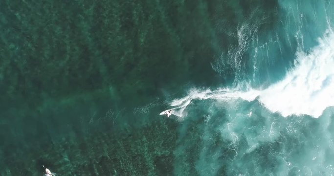 Top Down Aerial tracking shot on skilled male surfer riding a huge wave on a clear blue day at the ocean catching waves