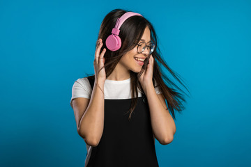 Pretty young asian girl with long hair having fun, smiling, dancing with headphones in studio against blue background. Music, dance, radio concept,