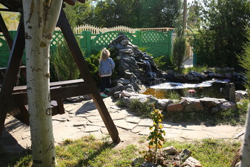 waterfall in its own courtyard in the summer against the backdrop of nature where pink lily blooms around and stones