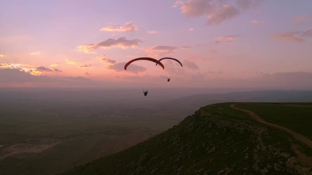 Two paragliders fly over mountain top in epic pink sunset light. Parachutes or paragliding experience. Adrenaline and extreme sport. Beautiful tranquil and calm time in nature