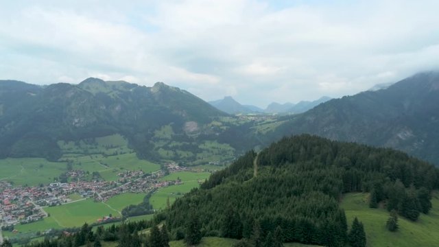 Majestic Aerial View of Village in Alps Mountains. Alpine Countryside with River, Forest and Car road. Nature, Agriculture and Ecotourism in Germany, Europe. 4K Drone Long Pull in Shot
