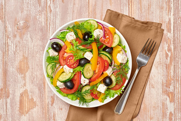 Greek salad with cucumeber, olives, feta cheese, cherry tomatoes, bell pepper, onion and lettuce. Diet, vitamin food. Healthy vegetarian meal concept. Tasty salad in bowl on wood, top view.