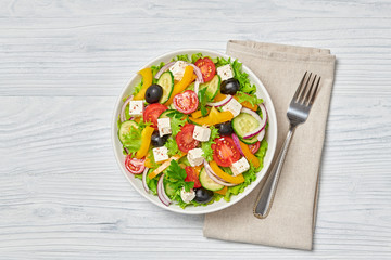 Greek salad with cucumeber, olives, feta cheese, cherry tomatoes, bell pepper, onion and lettuce. Diet, vitamin food. Healthy vegetarian meal concept. Tasty salad in bowl on wood, top view. Copy space
