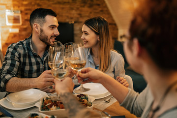 Young happy couple toasting with wine while having dinner with friends.