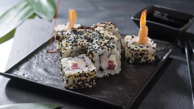Japenese sushi rolls with shrimps black caviar served on black plate in a restaurantt Asian chef pouring down two kinds of sour souces preparing traditional sushi meal. Healthy food traditions concept