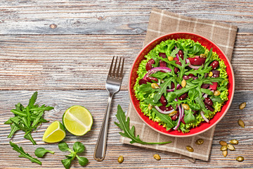 Vegan beetroot salad with red bean, lettuce, arugula, sunflower, sesame seed. Home made vegetarian beet salad. Clean eating concept on wood background. Tasty fresh beetroot veg dish. Top view.